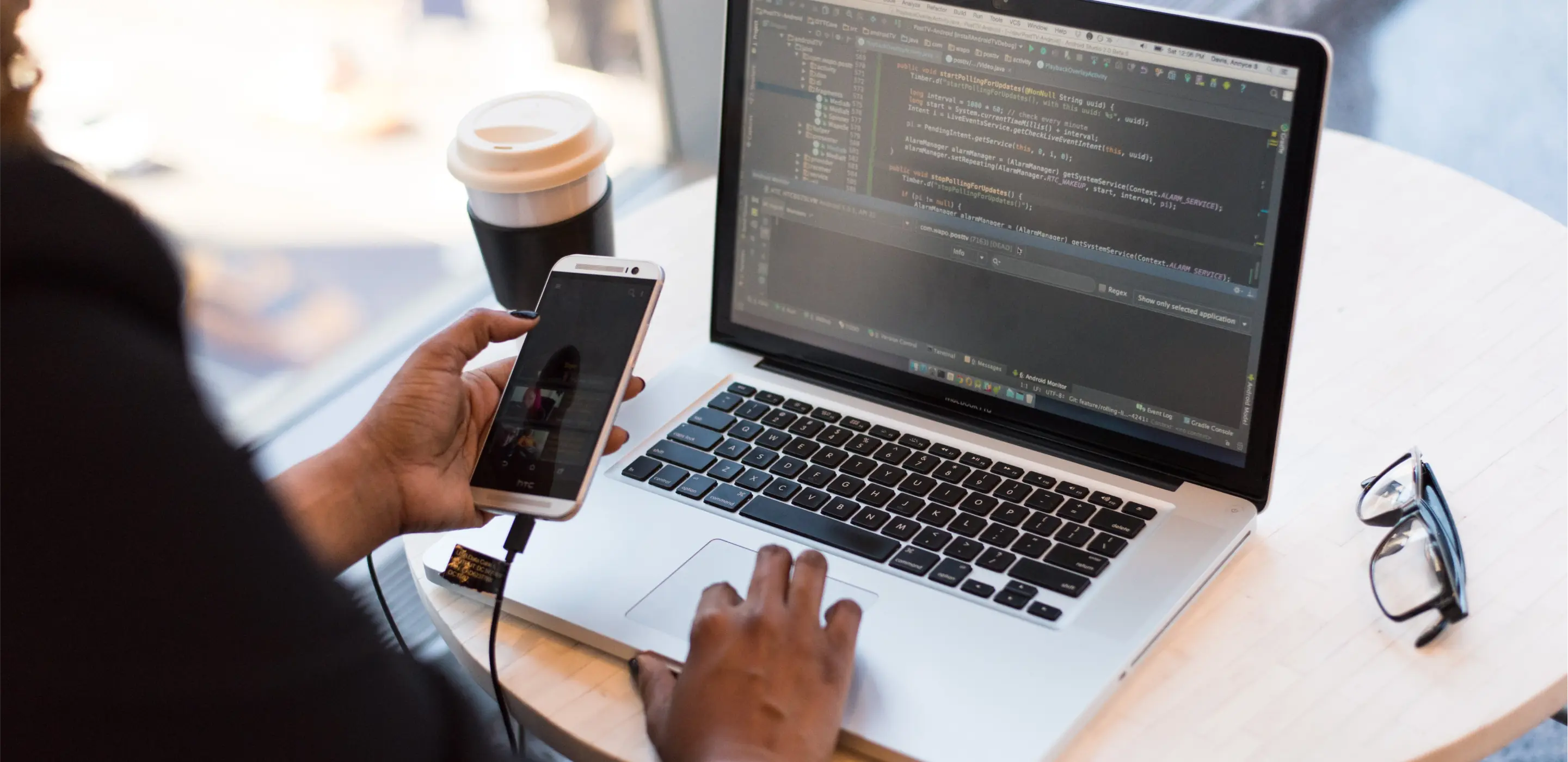 A person holding a mobile phone infront of their laptop, debuging thier mobile app