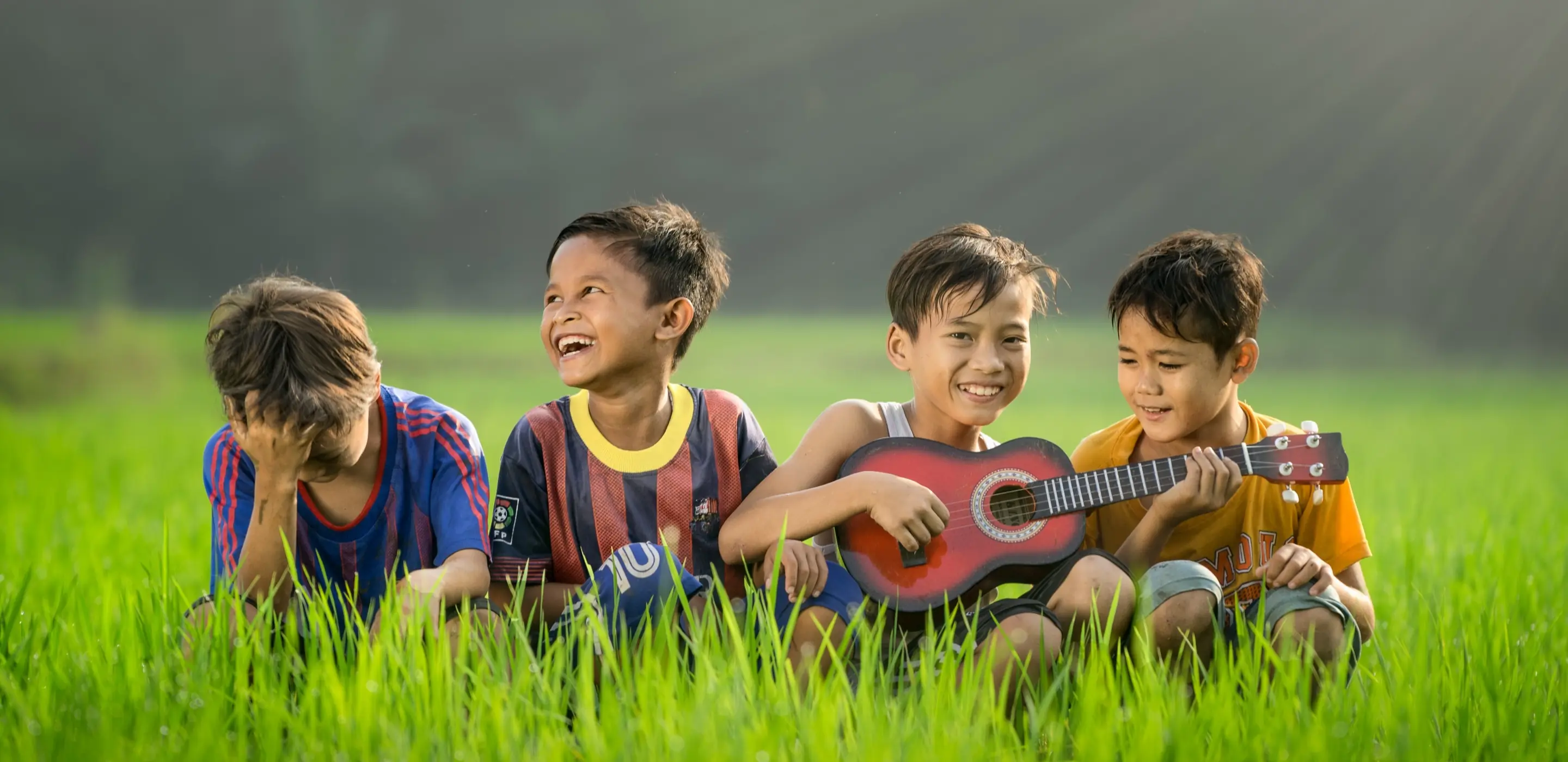 Four children smiling and playing banjo in open green field