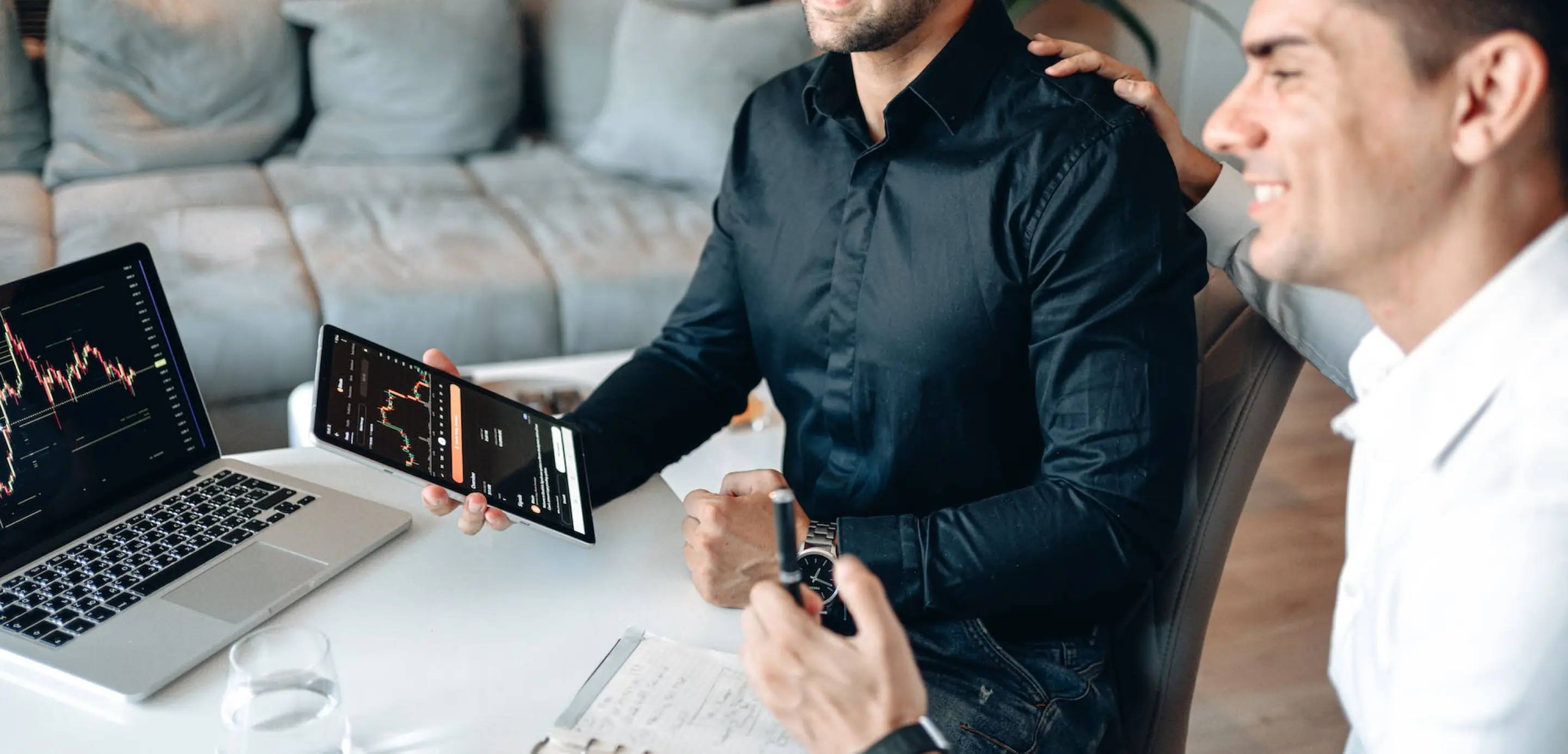 Two men infront of laptop discussing, one of them holding a tablet